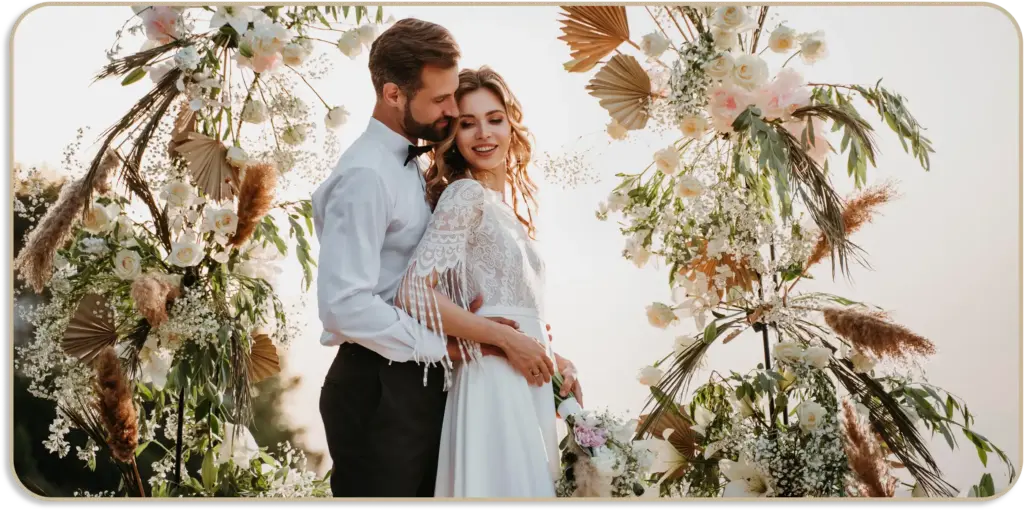 Elegante bruid en bruidegom poseren onder een luxe bloemenboog versierd met witte bloemen en decoratief groen.
